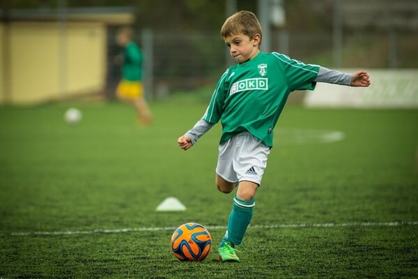 Kid playing football on the green pitch